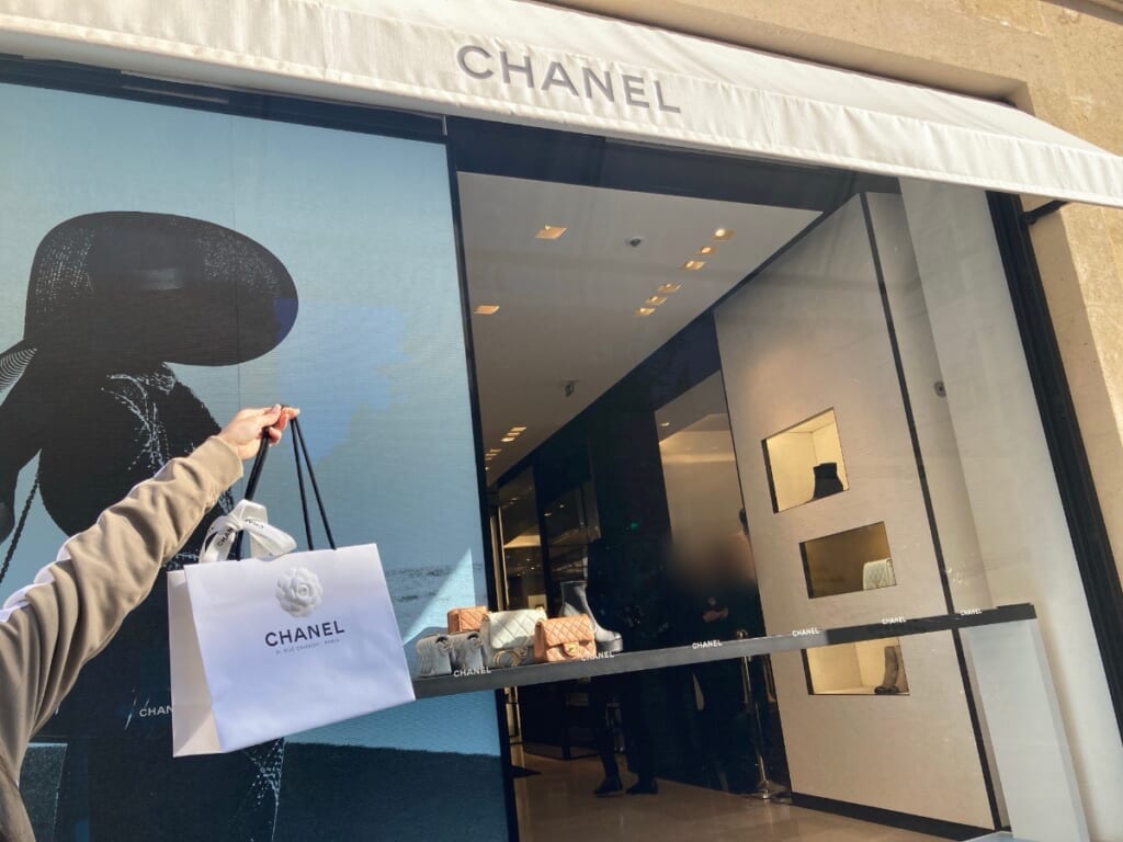 シャネルのお店の前で、白いショッピングバッグを持つ手